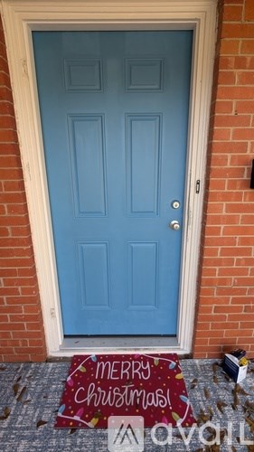 A blue door with a Merry Christmas mat in front.