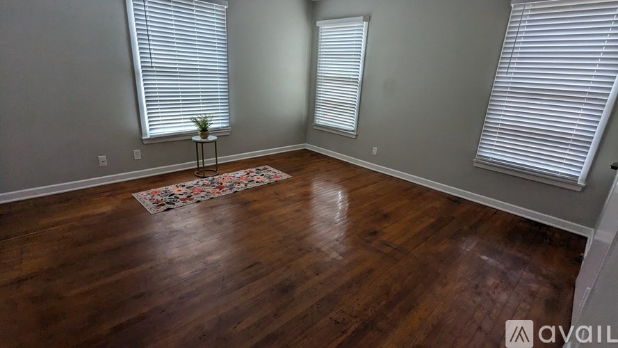 A room with wooden floors and two windows with blinds.