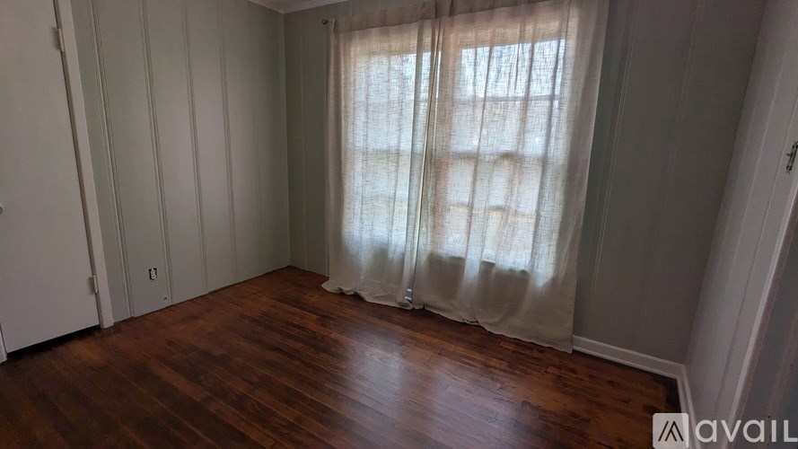 A room with wooden floors and a window with curtains.