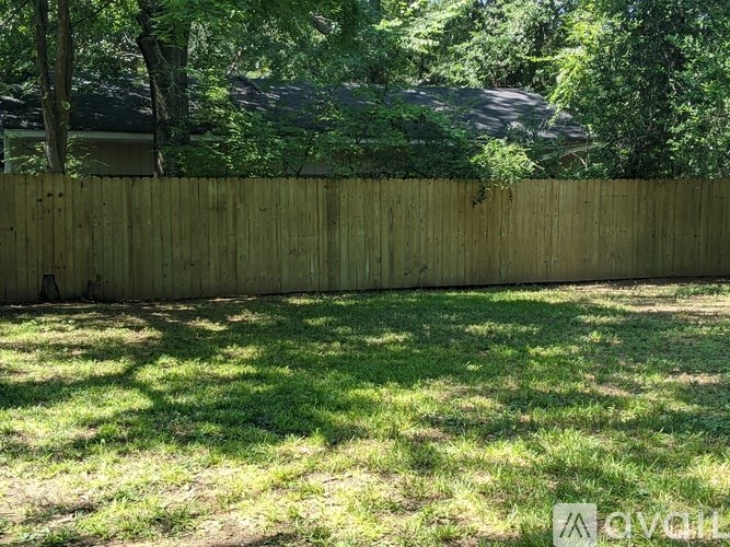 A wooden fence separates a grassy area from a wooded area.