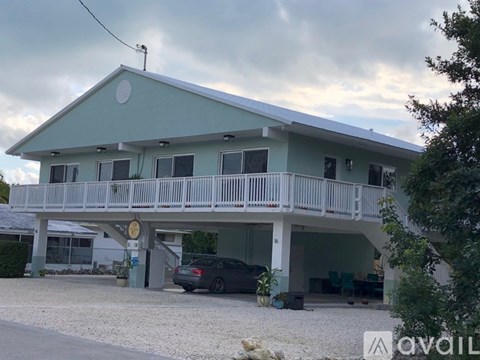 A car is parked in front of a two-story house with a balcony.