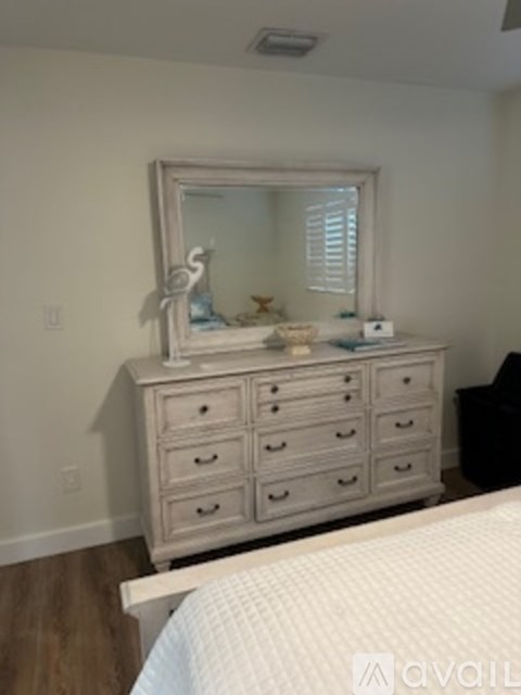 A white dresser with a mirror and a few items on top of it.