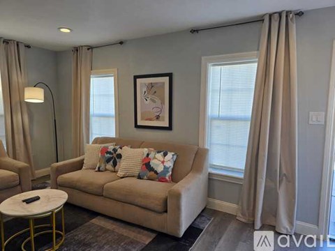 A living room with a beige couch, a small round table, and a painting on the wall.