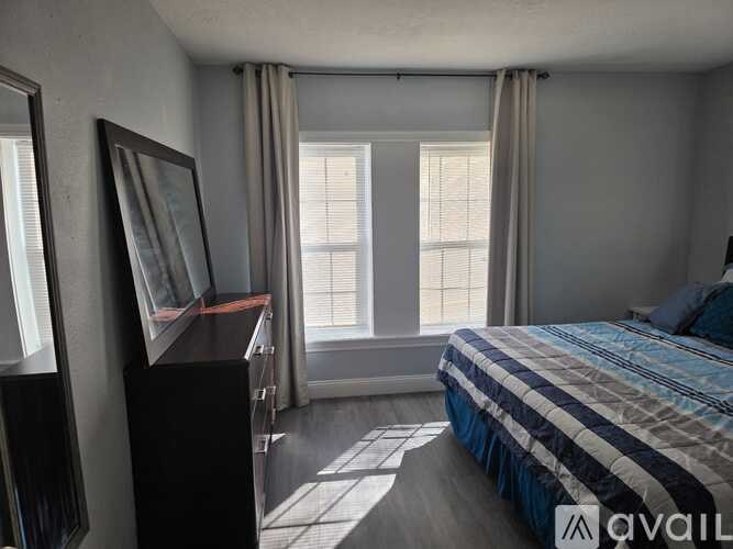 A bedroom with a bed, a dresser, and a window with curtains.
