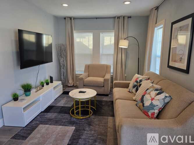 A living room with a beige couch, a white coffee table, and a flat-screen TV mounted on the wall.