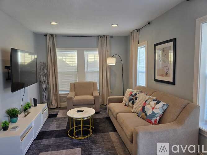 A living room with a beige couch, a white coffee table, and a flat-screen TV mounted on the wall.