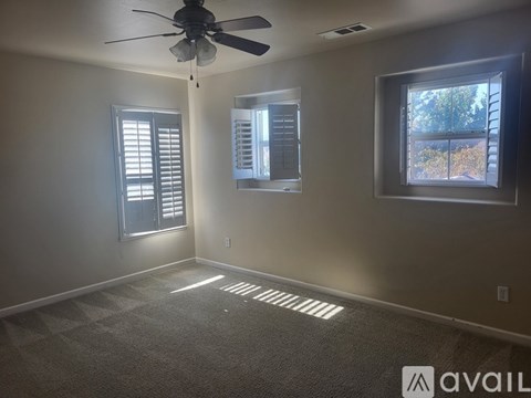 A room with a ceiling fan, two windows with blinds, and a carpeted floor.