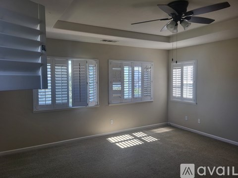 A room with a ceiling fan and two windows with blinds.