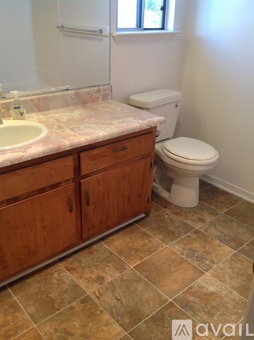 A bathroom with a toilet, sink, and wooden cabinets.