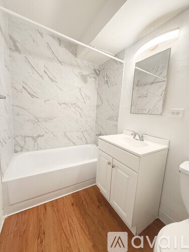 A bathroom with a white tub, sink, and wooden floor.
