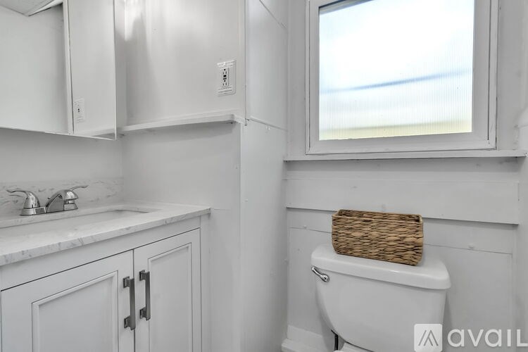 A white toilet with a basket on top sits next to a window in a bathroom.