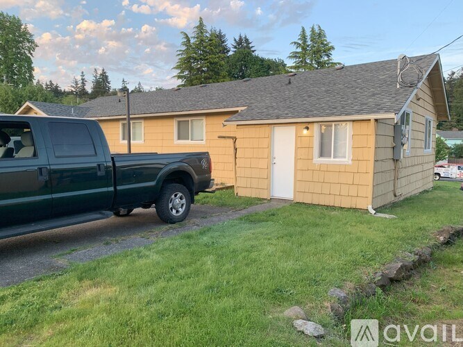 A green truck is parked in front of a yellow house.