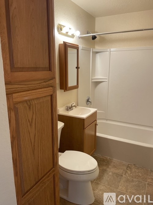A white toilet is in a bathroom with a wooden cabinet and a mirror above the sink.