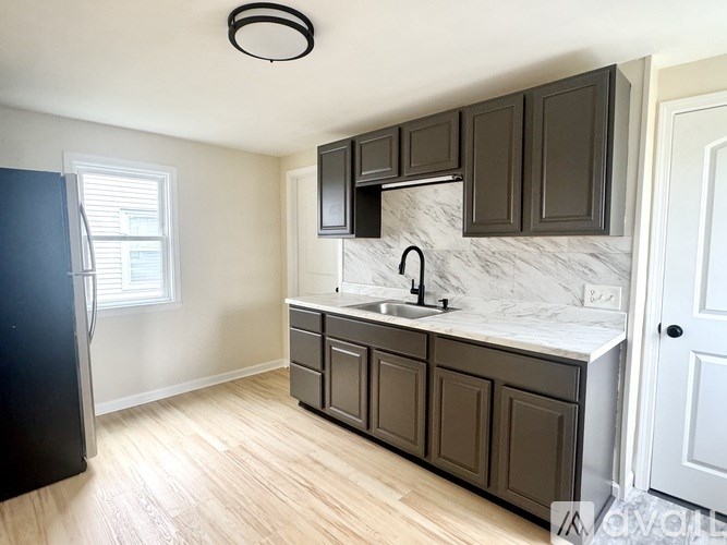 A kitchen with a black fridge, black cabinets, and a marble countertop.