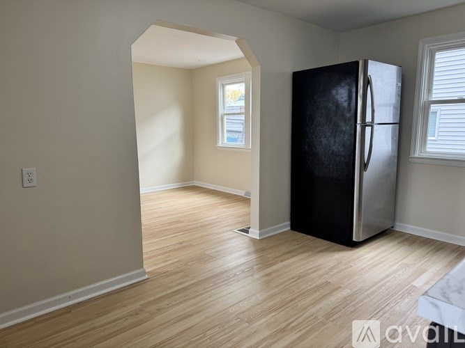 A black fridge stands in a room with wooden floors and a window.