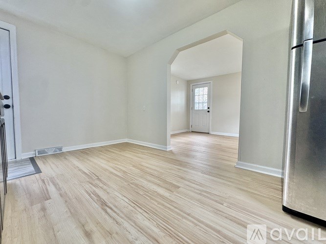 A room with wooden flooring and a refrigerator on the right side.