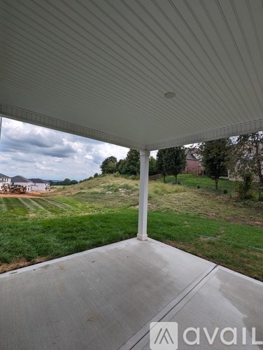 A patio with a white roof and a view of a green field and a house.