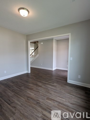 A room with wooden flooring and a staircase in the background.