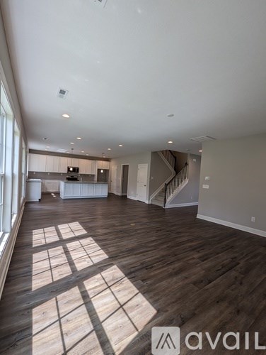 A spacious room with wooden floors and a staircase in the background.