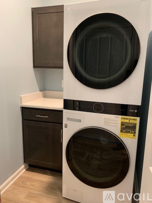 A white washing machine with a black door is in a room with a brown cabinet.