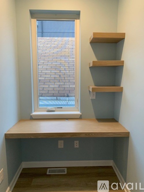 A window with a view of a brick wall is in a room with a window seat and shelves.