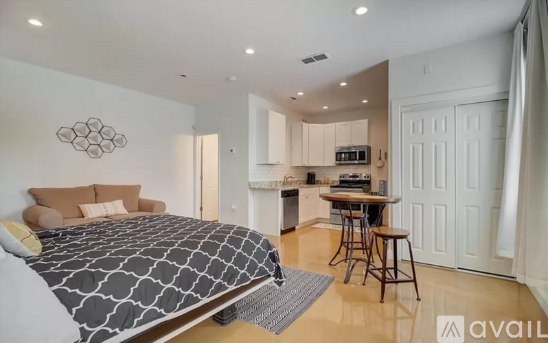 A bedroom with a large bed and a kitchen area in the background.