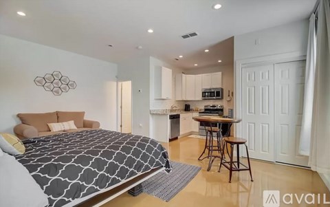 A bedroom with a large bed and a kitchen area in the background.