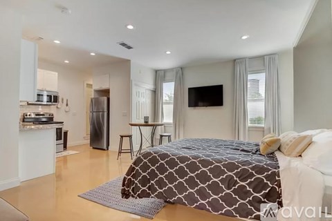 A bedroom with a large bed and a kitchen area in the background.