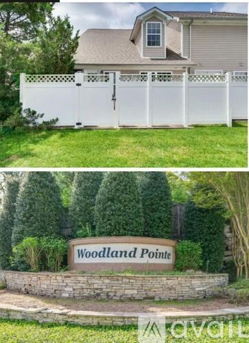 A sign that reads "Woodland Pointe" is in front of a white fence.