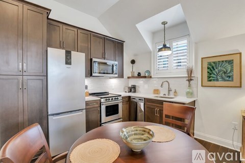 A kitchen with a table and chairs in the foreground and a refrigerator, microwave, oven, and sink in the background.