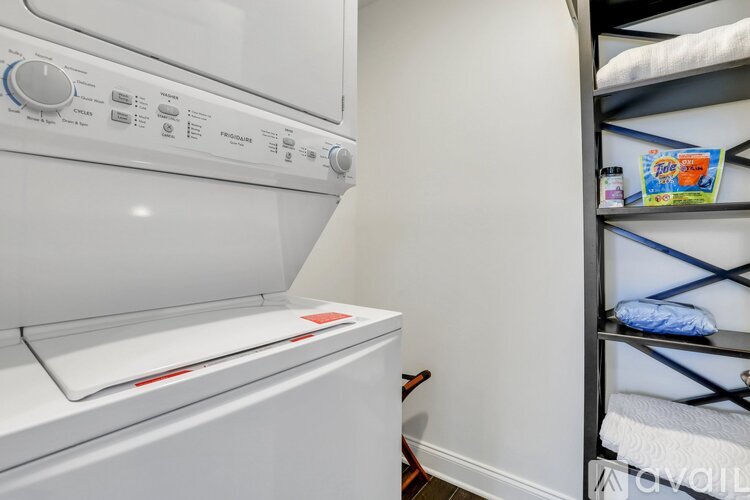 A white washing machine in a laundry room with a shelf to its right.