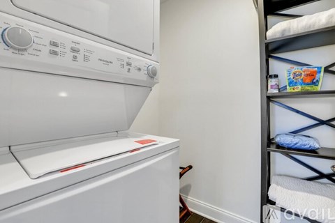 A white washing machine in a laundry room with a shelf to its right.