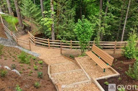 A wooden bench sits in a garden with a gravel path leading to a wooden fence.