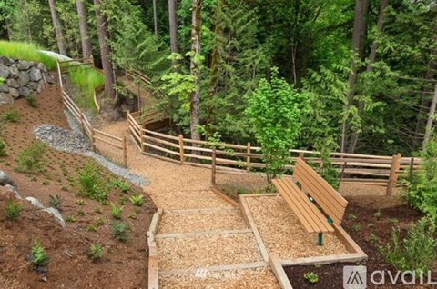 A wooden bench is situated in a garden with a gravel path leading to it.