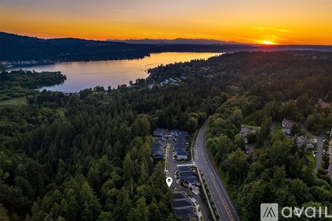A sunset view of a lake with a road and trees in the foreground.