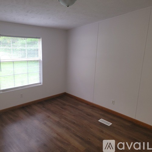 A room with wooden flooring and a window with blinds.
