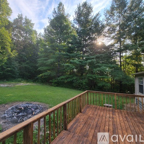 A wooden deck with a railing and a fire pit in the middle of a grassy area with trees in the background.