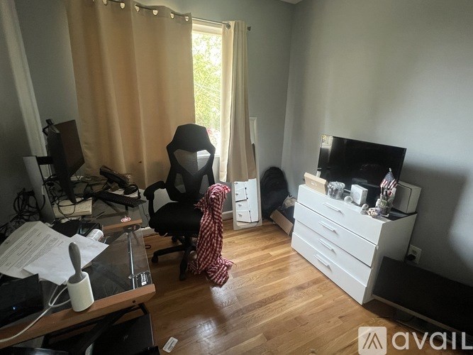 A room with a desk, chair, and a window with curtains.