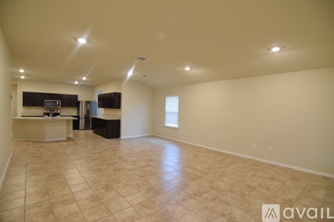 A spacious room with beige tiled flooring and a kitchen area with a counter and cabinets.