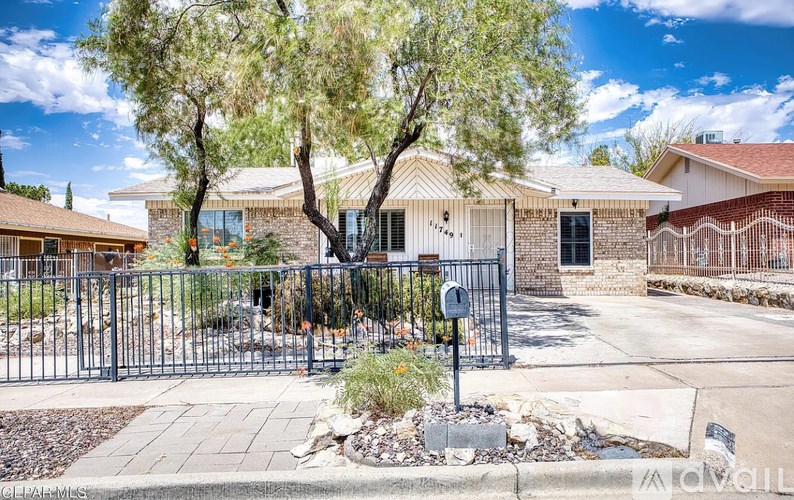 A gated entrance to a residential area with a sign and a tree.