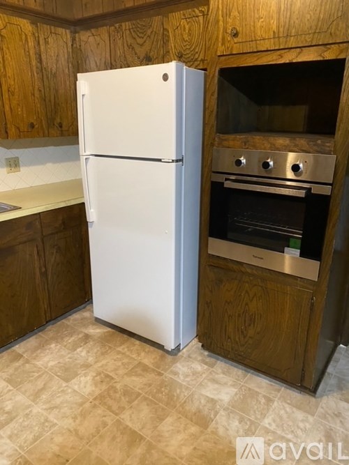 A white refrigerator stands next to a wooden cabinet with an oven underneath it.