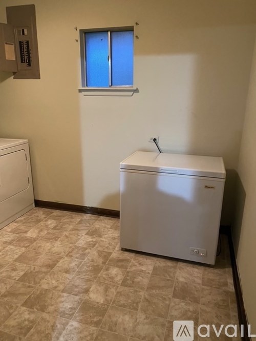 A small white washing machine in a room with a window.