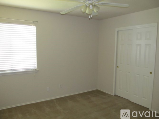 A room with a white door, a ceiling fan, and a window with blinds.
