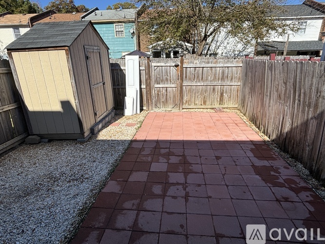A backyard with a wooden fence and a red tile walkway.