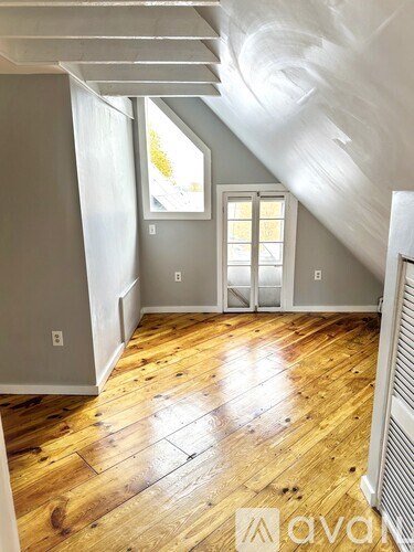 A room with wooden floors and a window with white curtains.