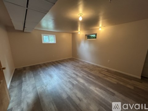 A room with wooden flooring and two windows.