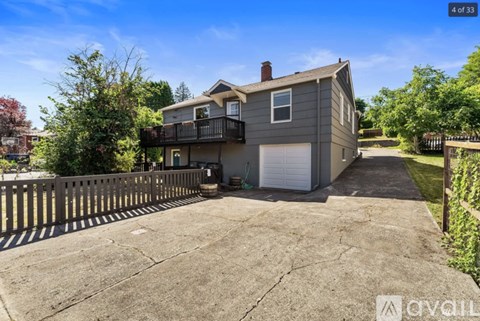 A house with a grey exterior and a white garage door is surrounded by a wooden fence.
