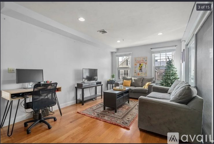 A living room with a grey couch, a black chair, a white desk, and a TV.