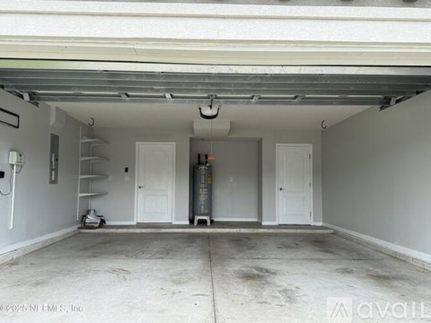A spacious garage with a white ceiling and walls, containing a shelving unit, a fire extinguisher, and a large cylindrical object.