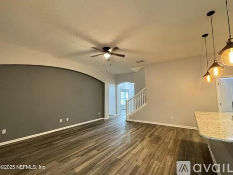 A room with a ceiling fan and a long wooden floor.